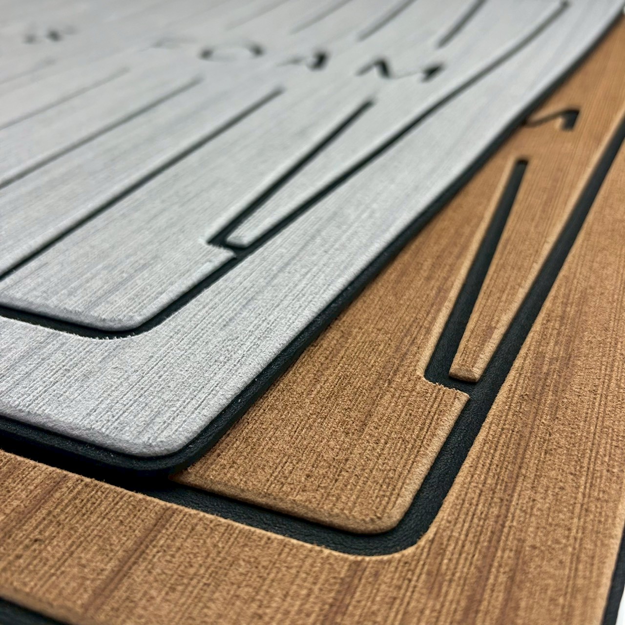 Close-up of laser-engraved wood grain texture on gray and teak-colored EVA teak decking sheet samples showing precise cut lines and material thickness